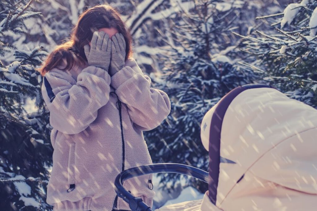 Ein Mutter mit Kinderwagen im Schnee schlägt sich verzweifelt die Hände vors Gesicht